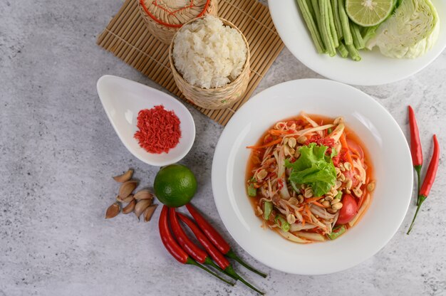 Insalata tailandese della papaia in un piatto bianco con riso appiccicoso in bambù del canestro di vimini e gamberetto essiccato