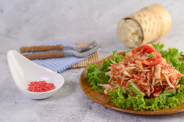 Insalata tailandese della papaia in un piatto di legno con riso appiccicoso e gamberetto essiccato