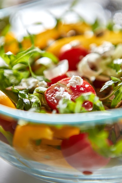 Insalata vitaminica estiva di rucola, pomodoro, porro e formaggio in una ciotola di vetro foto macro Cibo dietetico sano