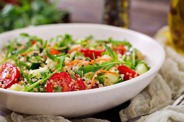 Insalate con quinoa, rucola, ravanello, pomodori e cetriolo in ciotola sul tavolo di legno. Cibo sano, dieta, disintossicazione e concetto vegetariano.
