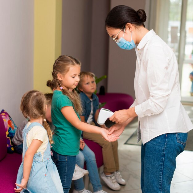 Insegnante che controlla la temperatura dei suoi studenti per la lezione durante il periodo di pandemia