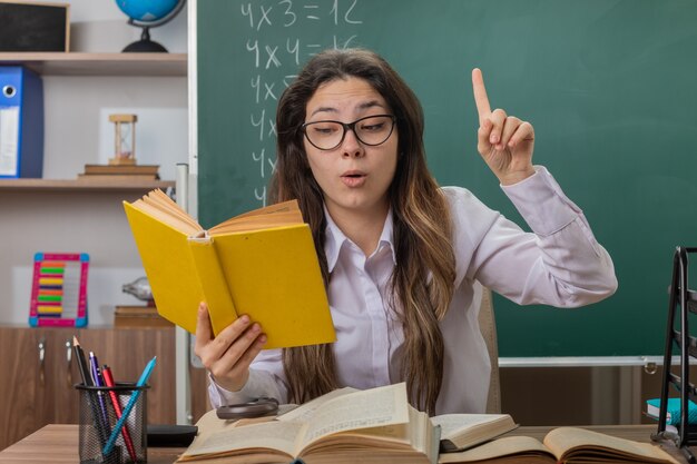 Insegnante di giovane donna con gli occhiali con lettura di libri che sembra incuriosito