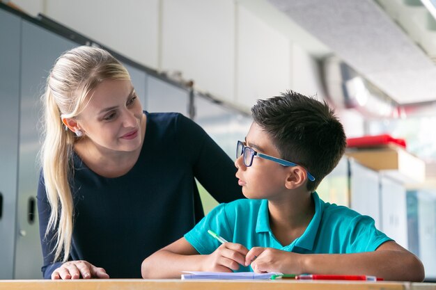 Insegnante di scuola allegro che dà aiuto e supporto allo scolaro in classe