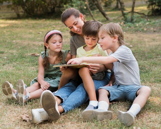 Insegnante di tiro completo e bambini seduti a terra