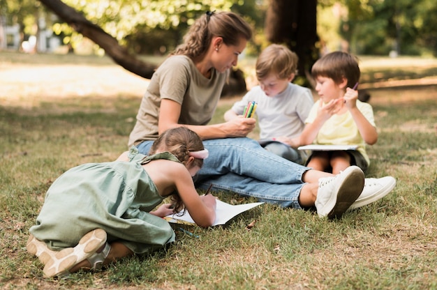 Insegnante e bambini seduti sull'erba a pieno tiro