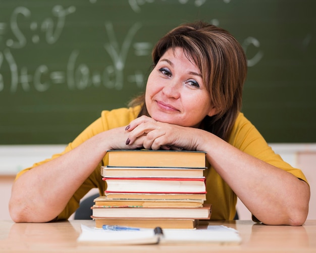 Insegnante femminile allo scrittorio che si siede sulla pila di libri