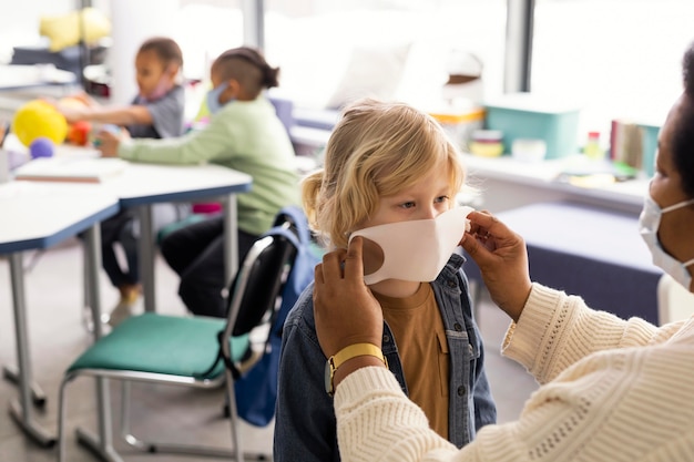 Insegnante femminile che aiuta i bambini con la loro mascherina medica