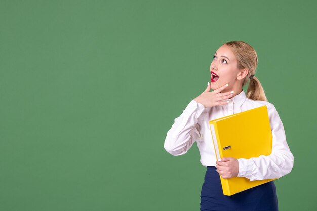 Insegnante femminile di vista frontale che posa con i file gialli su fondo verde libro di scuola della donna dell'uniforme dello studente del lavoro di lezione di studio della biblioteca