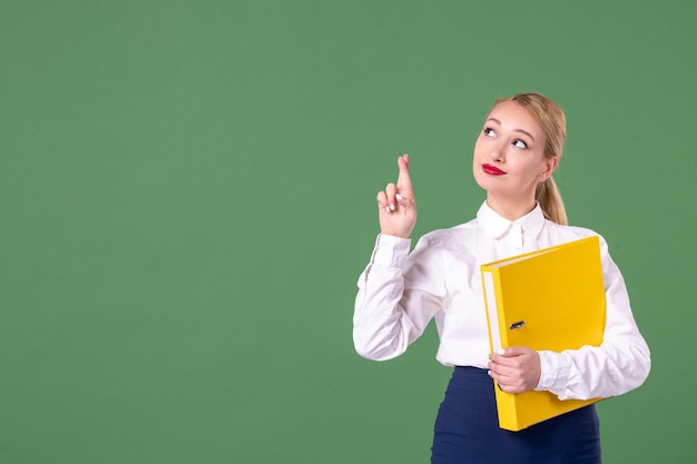 Insegnante femminile di vista frontale che posa con i file gialli su sfondo verde biblioteca lezione di studio studente universitario scuola uniforme libro lavoro