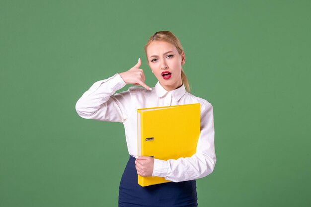 Insegnante femminile di vista frontale che posa in abiti rigorosi con file gialli su sfondo verde lavoro libro studente scuola università biblioteca lezione a colori