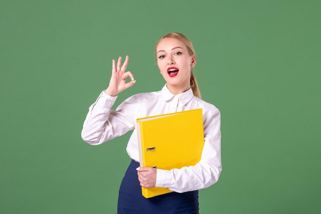 Insegnante femminile di vista frontale che posa in abiti rigorosi con file gialli su sfondo verde lavoro libro studente scuola università donna biblioteca lezione colori