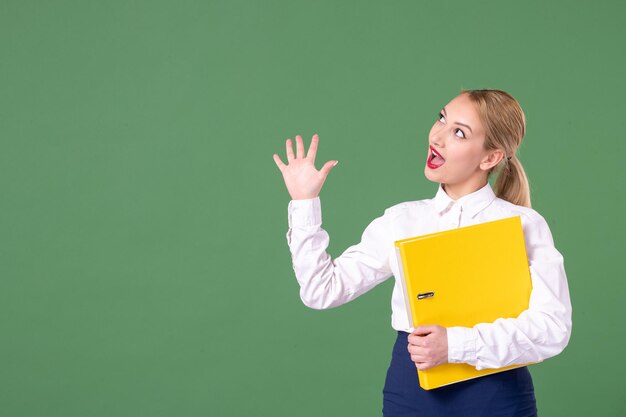 Insegnante femminile di vista frontale che tiene file gialli su sfondo verde studio uniforme donna lezione universitaria biblioteca libro studente lavoro scolastico