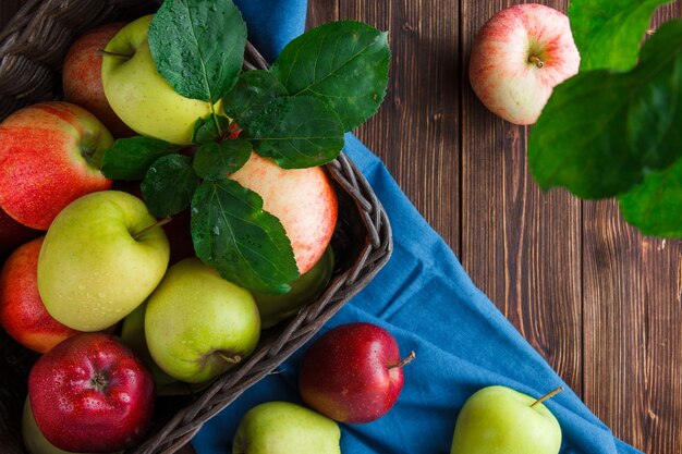 Insieme delle foglie e delle mele in una scatola su un panno blu e su un fondo di legno. disteso.