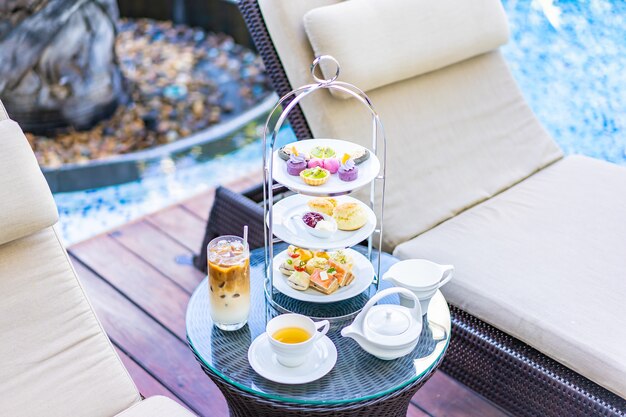 Insieme di tè di pomeriggio con caffè del latte e tè caldo sulla tavola vicino alla sedia intorno alla piscina