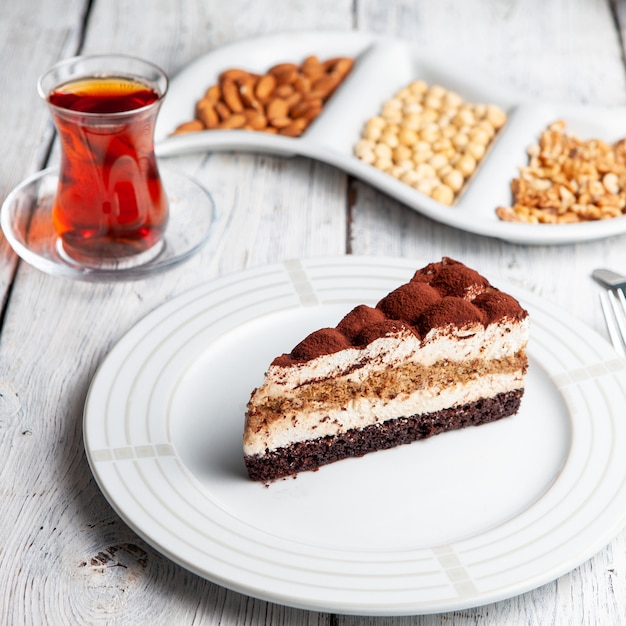Insieme di tè, noci e dessert delizioso in un piatto su un fondo di legno bianco. Veduta dall'alto.