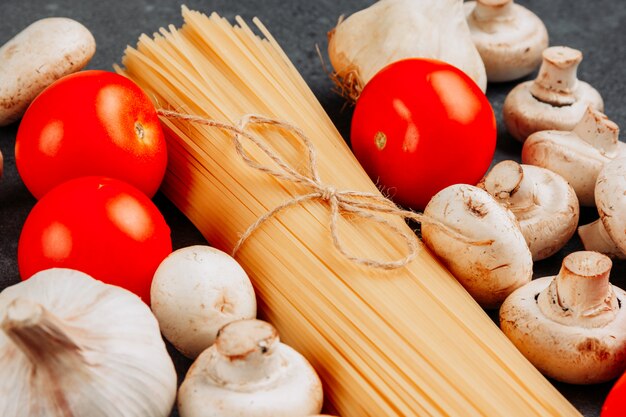 Insieme di un mazzo di pasta degli spaghetti e pomodori e funghi bianchi su un fondo strutturato grigio. Veduta dall'alto.