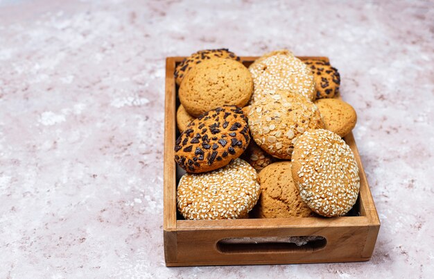 Insieme di vari biscotti di stile americano in vassoio di legno su fondo in cemento leggero. Frollini con semi di sesamo, burro di arachidi, fiocchi d'avena e biscotti con gocce di cioccolato.