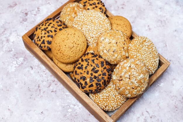 Insieme di vari biscotti di stile americano in vassoio di legno su fondo in cemento leggero. Frollini con semi di sesamo, burro di arachidi, fiocchi d'avena e biscotti con gocce di cioccolato.