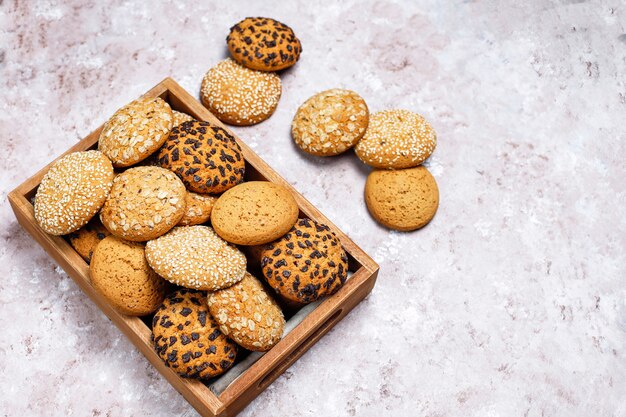 Insieme di vari biscotti di stile americano in vassoio di legno su fondo in cemento leggero. Frollini con semi di sesamo, burro di arachidi, fiocchi d'avena e biscotti con gocce di cioccolato.