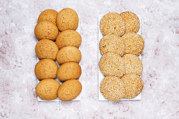 Insieme di vari biscotti in stile americano su uno sfondo di cemento chiaro. Frollini con coriandoli, semi di sesamo, burro di arachidi, fiocchi d'avena e biscotti al cioccolato.