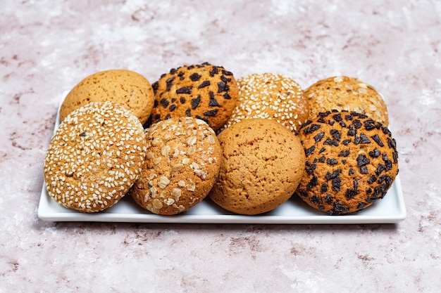 Insieme di vari biscotti in stile americano su uno sfondo di cemento chiaro. Frollini con coriandoli, semi di sesamo, burro di arachidi, fiocchi d'avena e biscotti al cioccolato.