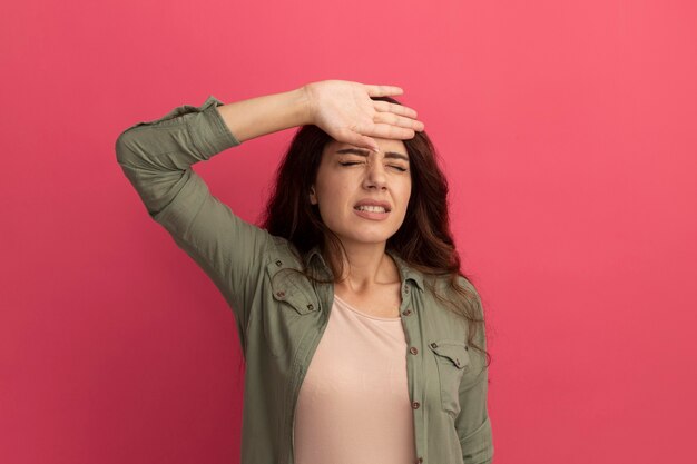 Insoddisfatto con gli occhi chiusi giovane bella ragazza che indossa la maglietta verde oliva che mette la mano sulla fronte isolata sulla parete rosa