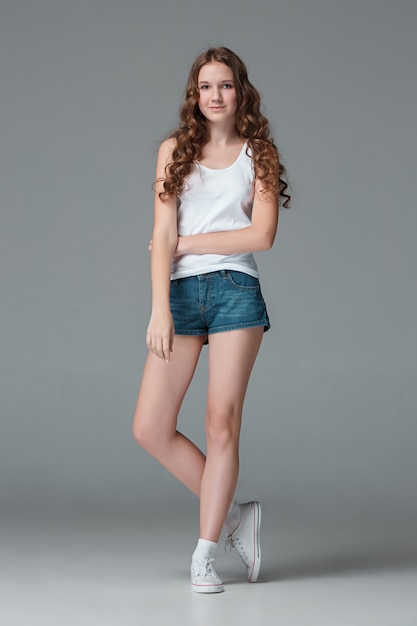 Integrale di giovane ragazza femminile esile negli shorts del denim sulla parete grigia
