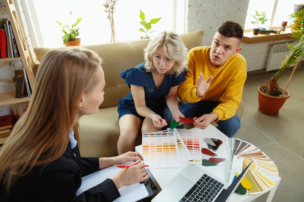 Interior designer che lavora con una giovane coppia. Bella famiglia e designer professionista o architetto che discute del concetto di interni futuri, lavorando con tavolozza dei colori, disegni di stanze in un ufficio moderno