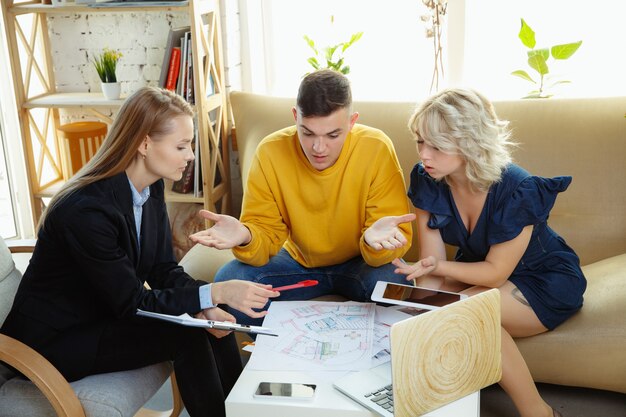 Interior designer che lavora con una giovane coppia. Bella famiglia e designer professionista o architetto che discute del concetto di interni futuri, lavorando con tavolozza dei colori, disegni di stanze in un ufficio moderno