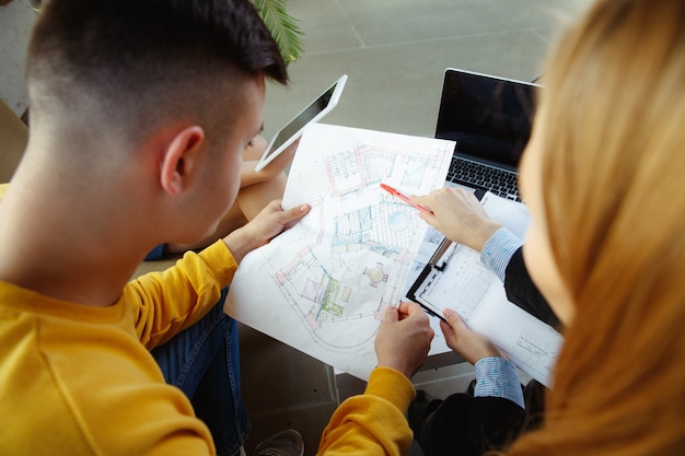 Interior designer che lavora con una giovane coppia. Bella famiglia e designer professionista o architetto che discute del concetto di interni futuri, lavorando con tavolozza dei colori, disegni di stanze in un ufficio moderno