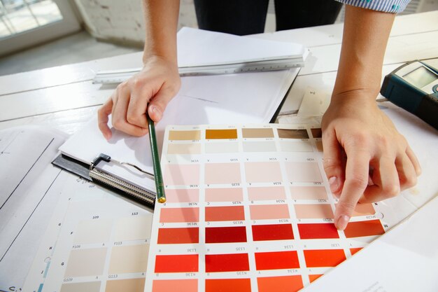 Interior designer professionista o architetto che lavora con la tavolozza dei colori, i disegni delle stanze in un ufficio moderno. Giovane modello femminile che pianifica futuro appartamento o casa, scegliendo colori e derocation