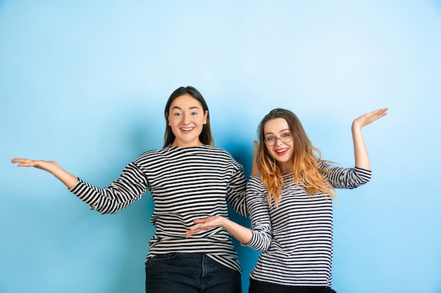 Invitante, saluto. Giovani donne emotive isolate sul muro blu sfumato. Concetto di emozioni umane, esperienza facciale, amicizia, annuncio. Bellissimi modelli caucasici in abiti casual.