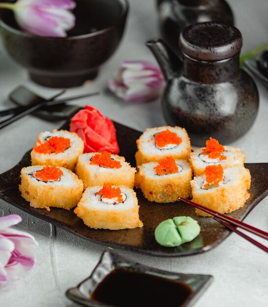 Involtini croccanti con caviale rosso, zenzero e wasabi su un piatto nero.