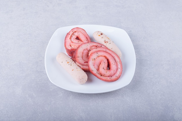 Involtini di carne affumicata e salsicce sul piatto bianco.