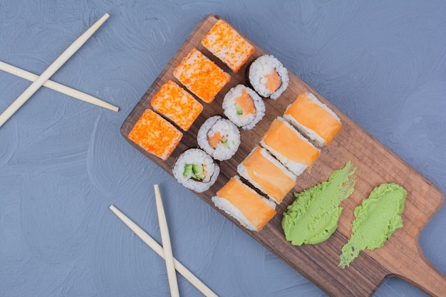 Involtini di maki Philadelphia, salmone e sake con wasabi su un piatto di legno.