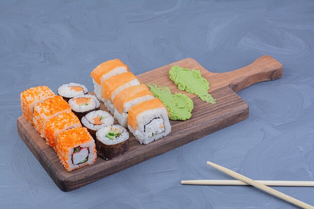 Involtini di maki Philadelphia, salmone e sake con wasabi su un piatto di legno.