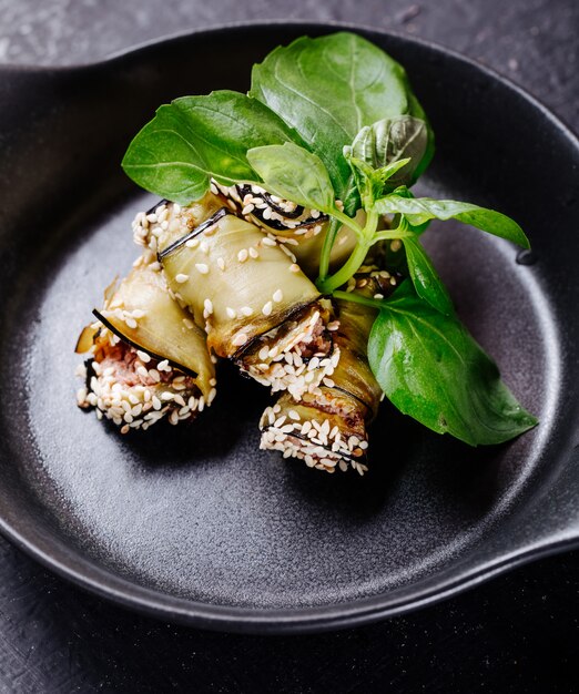 Involtini di melanzane con foglie di basilico all'interno della padella nera.