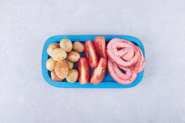 Involtini di prosciutto, pomodori e patate fritte sul piatto blu.