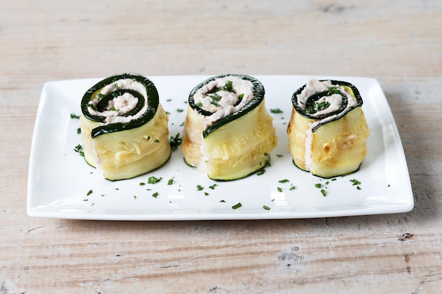 Involtini di zucchine alla griglia ripieni di crema di formaggio e tonno su tavola di legno