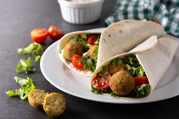 Involucro di tortilla con falafel e verdure su fondo di pietra nera