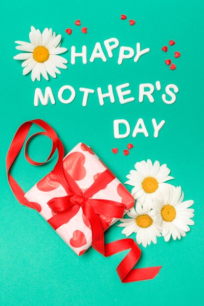 Iscrizione di giorno di madri felice vicino a fiori bianchi e scatola regalo