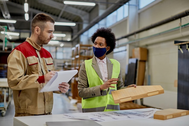 Ispettore afroamericano che parla con il lavoratore mentre esamina il legno lavorato in una fabbrica
