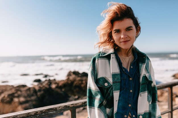 Ispirato ragazza caucasica in posa davanti alla telecamera in una giornata ventosa sul mare Foto all'aperto di donna bionda emotiva in camicia spogliata in posa sullo sfondo della natura