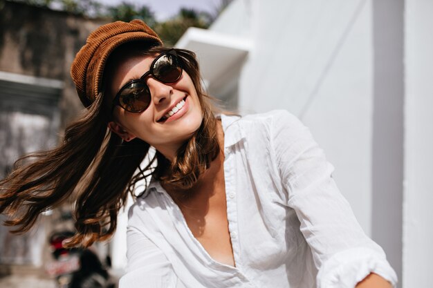Istantanea della donna che gode della giornata di sole estivo all'esterno. Ragazza in camicia alla moda e cappello sorridente.