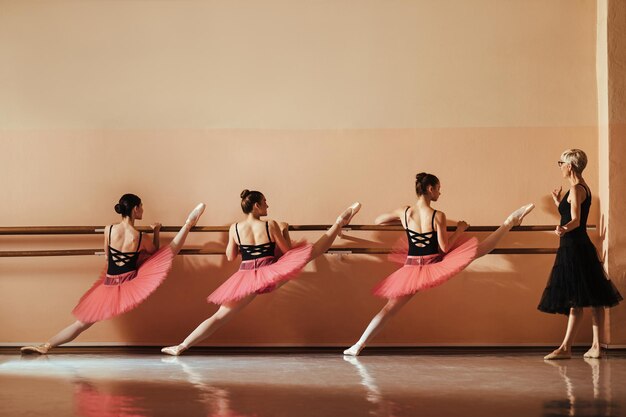 Istruttore di balletto maturo che tiene una classe a un gruppo di ballerine che stanno facendo esercizi di stretching su una sbarra in studio di danza Spazio di copia