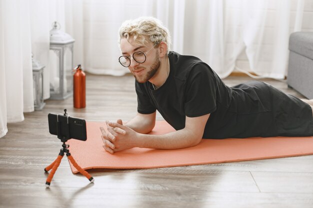 Istruttore di fitness o video blogger che fa stretching. L'uomo si sta riprendendo con la fotocamera dello smartphone a casa.