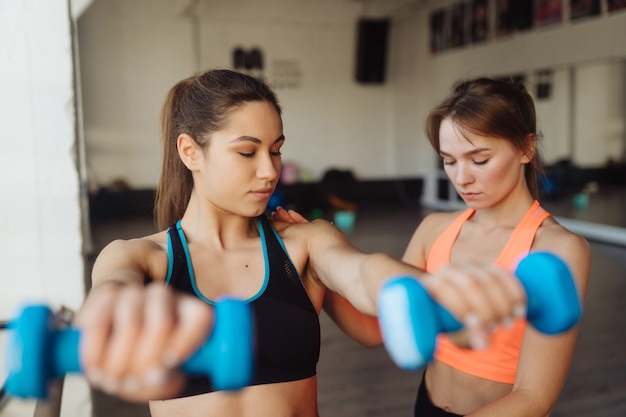 Istruttore personale della giovane donna che aiuta con l'allenamento in palestra. Donna che fa esercizi