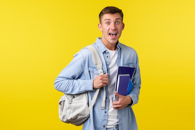 Istruzione, corsi e concetto di università. Sorpreso ragazzo sorridente felice che vede qualcosa di stupito mentre si dirige in classe al college o al collegio, tenendo in mano lo zaino con i quaderni.