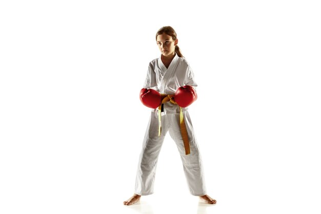 Junior fiducioso in kimono che pratica combattimento corpo a corpo, arti marziali. Giovane combattente femminile con l'addestramento della cintura gialla sulla parete bianca. Concetto di stile di vita sano, sport, azione.