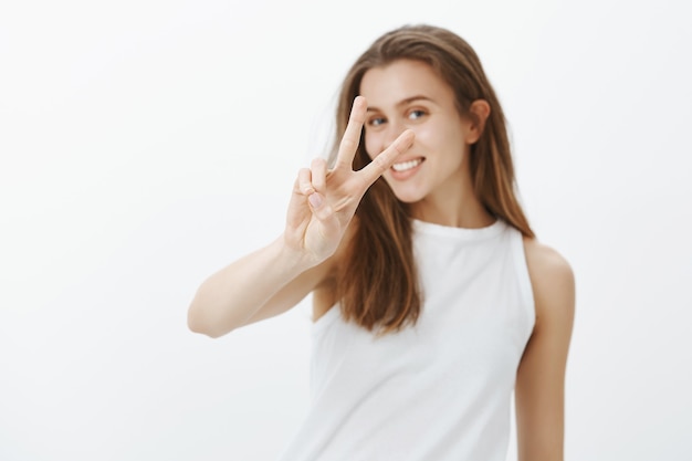 Kawaii giovane donna caucasica che mostra gesto di pace e sorridente con denti bianchi